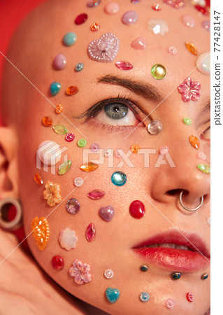 Unladylike woman with piercing and decor at her face looking at up with serious expression Unladylike woman with piercing and decor at her face looking at up with serious expression 77428147