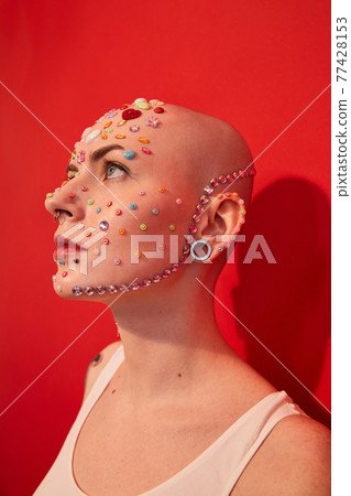 Mannish female with piercing and decor at her face looking away Mannish female with piercing and decor at her face looking away 77428153