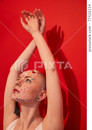 Masculine woman with decor at her face looking at her hands while keeping it over her head 77428154