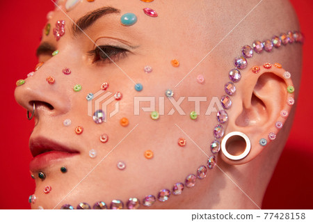 Mannish woman with decor of rhinestones at her face posing over the red background Mannish woman with decor of rhinestones at her face posing over the red background 77428158