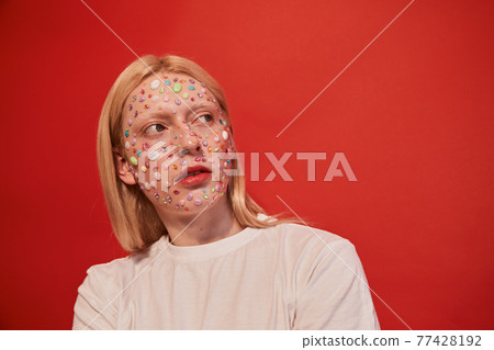 Feminine man with rhinestones at his face that accentuate his unusual appearance looking away 77428192