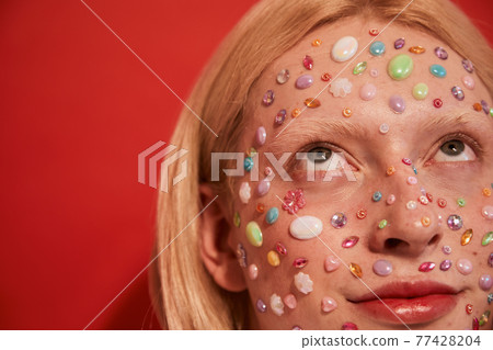 Blonde long haired man looking away while posing with rhinestones at his face 77428204