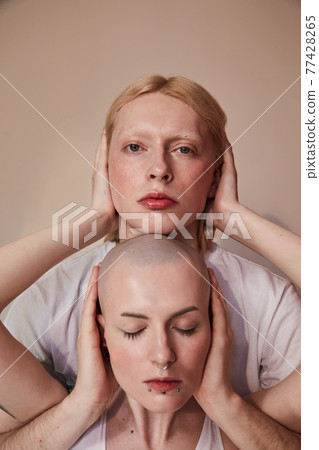 Long haired man and bald masculine woman standing and hiding ears of each other Long haired man and bald masculine woman standing and hiding ears of each other 77428265