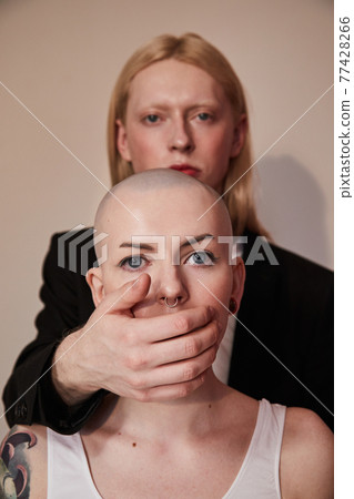 Man standing behind the bald masculine woman and hiding her mouth Man standing behind the bald masculine woman and hiding her mouth 77428266