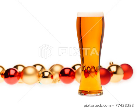 Tall glass of ale or beer with christmas baubles in background on white 77428388