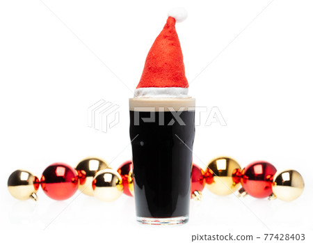 Dark ale beer in pint glass with christmas red hat and christmas baubles on white background 77428403