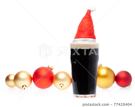 Dark ale beer in pint glass with christmas red hat and christmas baubles on white background 77428404