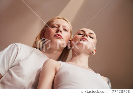 Woman with piercing at her face posing near the womanly albino guy with feminine features Woman with piercing at her face posing near the womanly albino guy with feminine features 77428708