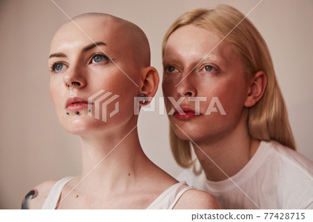 Womanly albino man with long blonde hair posing nearby bald masculine female Womanly albino man with long blonde hair posing nearby bald masculine female 77428715