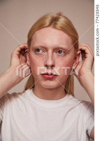 Albino feminine man tucks his hair behind ears while posing in studio 77428848