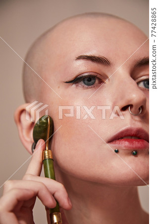 Woman using a jade massage roller on her cheek on the beige background Woman using a jade massage roller on her cheek on the beige background 77428865