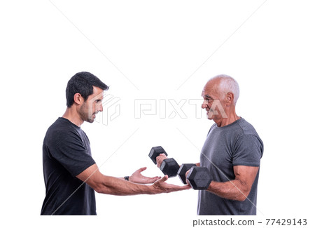 Elderly male client exercising with a fitness trainer, lifts dumbbells. On a white isolated background. 77429143