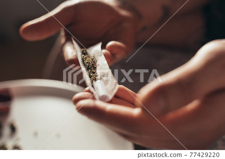 Man sitting at the table and holding special paper with filter and cannabis Man sitting at the table and holding special paper with filter and cannabis 77429220