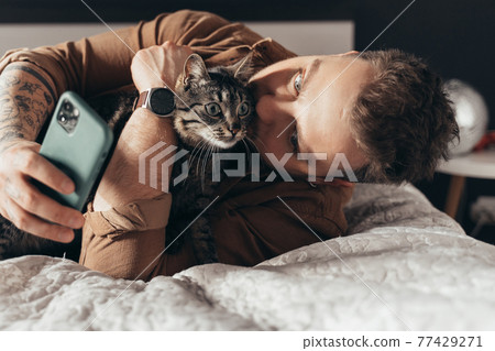 Man laying at the bed with his cat and making selfie 77429271
