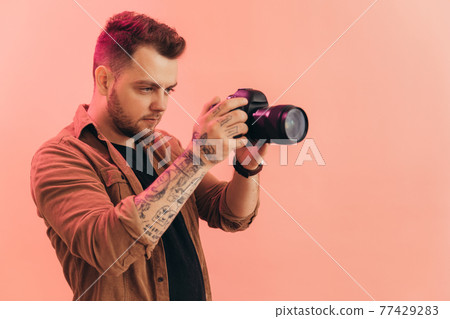 Man exposing frame with professional camera while standing behind the pink wall Man exposing frame with professional camera while standing behind the pink wall 77429283