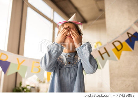 Girl closed her eyes while grimaces into the camera at home during her birthday 77429892