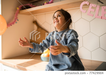 Girl catching a balloon while sitting at the working area at the kitchen 77429984