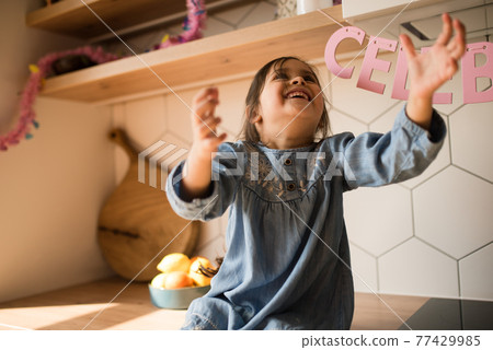 Girl catching a balloon while sitting at the working area at the kitchen Girl catching a balloon while sitting at the working area at the kitchen 77429985
