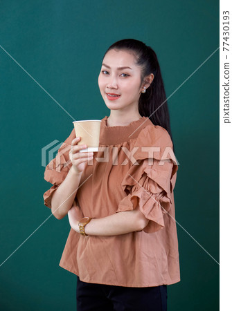 Young asian woman in casual dress with a smile holding coffee drink in paper cup. Portrait on green background with studio light. Young asian woman in casual dress with a smile holding coffee drink in paper cup. Portrait on green background with studio light. 77430193