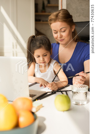 Kid and mother watching at the notebook while studying and doing homework at home 77430635