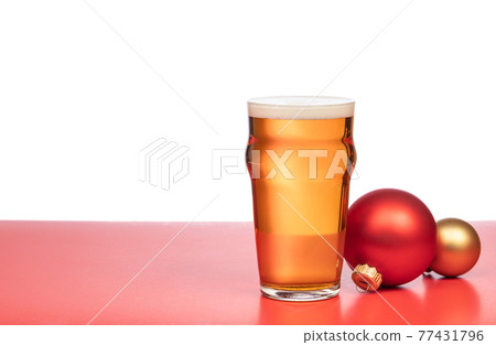 Pint glass of ale or beer with christmas baubles on red background Pint glass of ale or beer with christmas baubles on red background 77431796