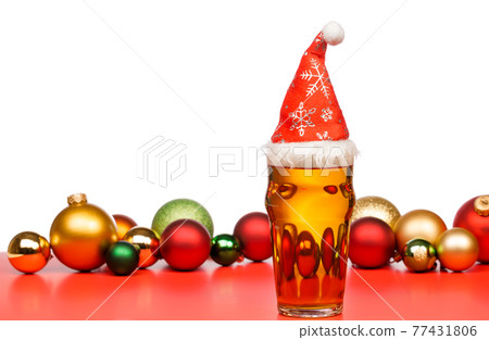 Pint glass of ale or beer with christmas red hat and baubles on red background Pint glass of ale or beer with christmas red hat and baubles on red background 77431806