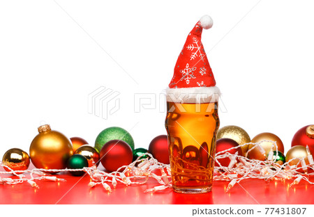 Pint glass of ale or beer with christmas red hat lights and baubles on red background Pint glass of ale or beer with christmas red hat lights and baubles on red background 77431807