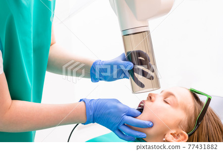 Elementary age girl receiving dental radiography or X-Ray in pediatric dental clinic Elementary age girl receiving dental radiography or X-Ray in pediatric dental clinic 77431882