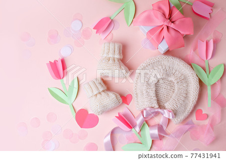 Bonnet and booties on a pink background. Handmade clothes for a newborn, decorative paper flowers. Newborn baby gift concept, mom's day, first birthday, first wardrobe, outfit 77431941