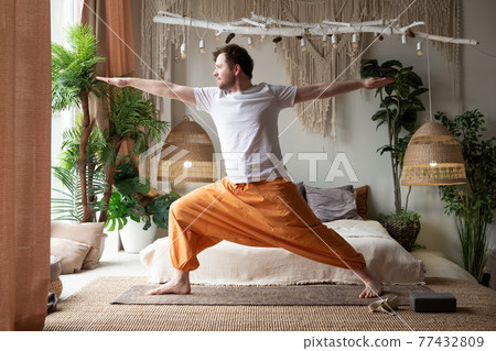man practicing yoga doing warrior pose or virabhadrasana at home 77432809