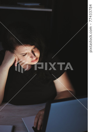 Young tired woman doing overtime job at night 77433784