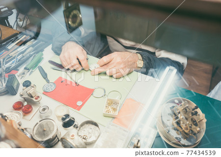 Top-down view on hands of watchmaker sitting at his workbench Top-down view on hands of watchmaker sitting at his workbench 77434539