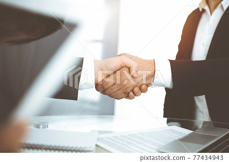 Unknown diverse business people are shaking hands finishing contract signing in sunny office, close-up. Business handshake concept 77434943
