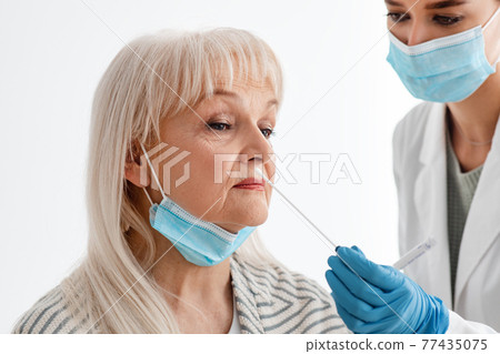 Doctor taking PCR test sample from potentially infected senior woman 77435075