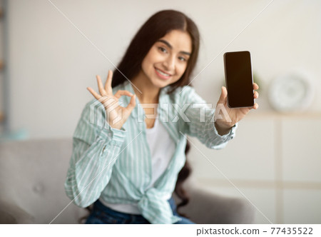 Charming Indian woman showing cellphone with empty screen, gesturing OK at home, mockup for website design Charming Indian woman showing cellphone with empty screen, gesturing OK at home, mockup for website design 77435522