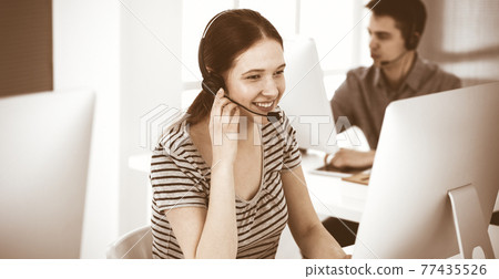Casual dressed young woman using headset and computer while talking with customers online. Group of operators at work. Call center, business concept Casual dressed young woman using headset and computer while talking with customers online. Group of operators at work. Call center, business concept 77435526