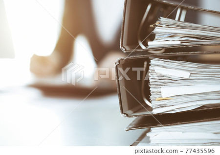 Binders with papers are waiting to be processed by business woman or bookkeeper working at the desk in office back in blur. Audit and tax concept Binders with papers are waiting to be processed by business woman or bookkeeper working at the desk in office back in blur. Audit and tax concept 77435596