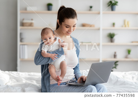 Modern Motherhood Concept. Young Woman Working On Laptop And Holding Newborn Baby Modern Motherhood Concept. Young Woman Working On Laptop And Holding Newborn Baby 77435598