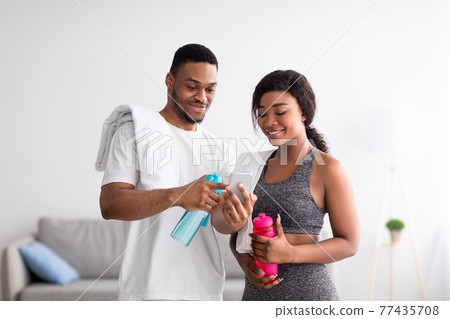 Millennial African American couple taking break from home training, watching online sports tutorial on cellphone 77435708