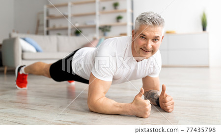 Domestic workout. Sporty mature man standing in elbow plank and strengthening abs muscles, doing fitness training 77435798