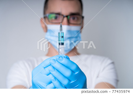A doctor in a medical mask and gloves holds a syringe with a coronavirus vaccine and a vaccine chip inside. Conspiracy theory. Chipping people A doctor in a medical mask and gloves holds a syringe with a coronavirus vaccine and a vaccine chip inside. Conspiracy theory. Chipping people 77435974