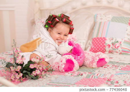 Adorable little girl with hair curlers hugs her favorite teddy bear toy 77436048