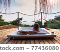 A handsome adult man lies in a hot tub at a luxurious exotic spa resort hotel balcony with sea and sunset view. 77436080