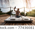 A handsome adult man taking selfie in a hot tub at a luxurious exotic spa resort hotel balcony with sea and sunset view. 77436081