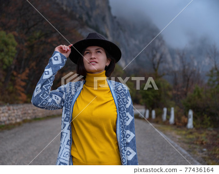 Stylish hipster woman in a hat walking down a mountain road Stylish hipster woman in a hat walking down a mountain road 77436164