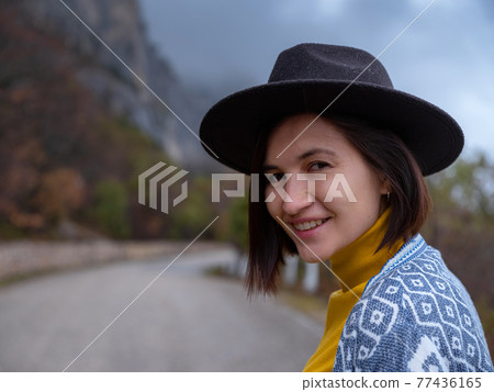Stylish hipster woman in a hat walking down a mountain road Stylish hipster woman in a hat walking down a mountain road 77436165