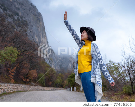 Stylish hipster woman in a hat walking down a mountain road Stylish hipster woman in a hat walking down a mountain road 77436166