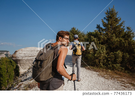 Two Men walking on rocky slope carrying Backpacks using trekking Sticks. Two Men walking on rocky slope carrying Backpacks using trekking Sticks. 77436173
