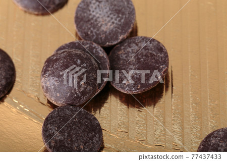 Round chocolate chips on a golden surface. Round chocolate chips on a golden surface. 77437433