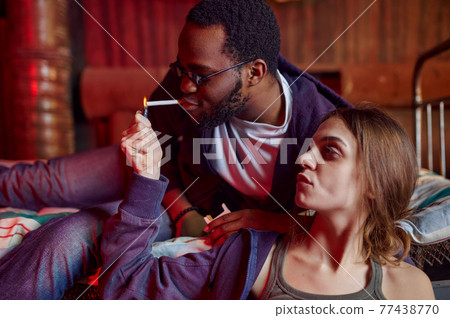Drug addicts smokes a cigarette while high in den Drug addicts smokes a cigarette while high in den 77438770